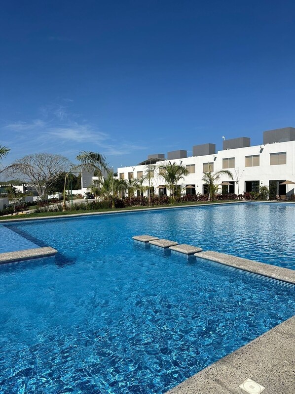 A swimming pool with clear blue water, surrounded by a white building with multiple windows and balconies.