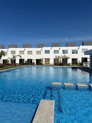 A swimming pool with a clear blue water surface, surrounded by a white building with multiple windows and balconies.
