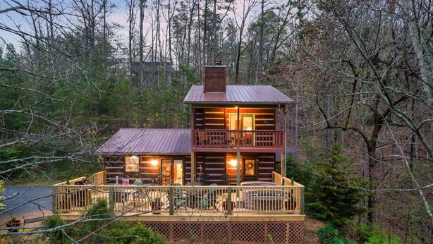A two-story log cabin with a deck and a covered porch, surrounded by forest. - Tree House Tranquility Cabin Close to Dollywood (Sevierville)