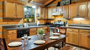 A wooden cabin kitchen with a dining table set for four, a stove, and a sign that reads "WELCOME TO THE CABIN". - Tree House Tranquility Cabin Close to Dollywood (Sevierville)