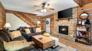 A cozy living room with a fireplace, leather sofa, wooden coffee table, and a bookshelf. - Tree House Tranquility Cabin Close to Dollywood (Sevierville)