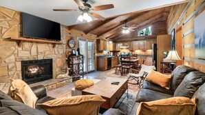 A cozy living room with a stone fireplace, leather sofa, and a dining area with wooden furniture. - Tree House Tranquility Cabin Close to Dollywood (Sevierville)