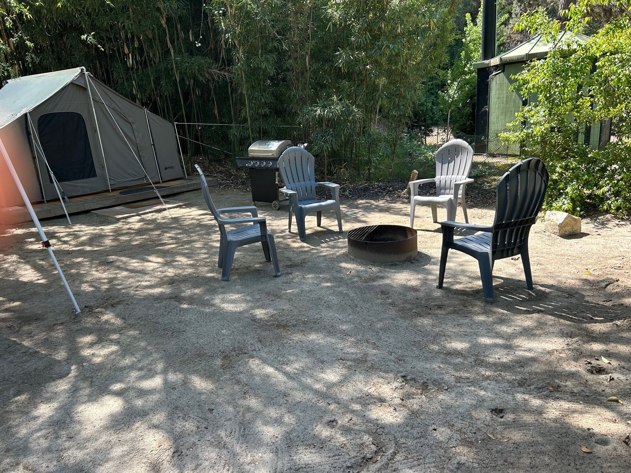 Een camping met een tent, twee Adirondack-stoelen, een vuurkorf en een draagbare barbecue.