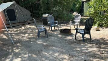Een camping met een tent, twee Adirondack-stoelen, een vuurkorf en een draagbare barbecue.