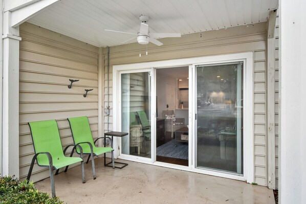 A covered patio with two green chairs, a ceiling fan, and a sliding glass door leading to an interior space. - Main Level Stepless Entry- Remodeled Condo (Saint Simons Island)