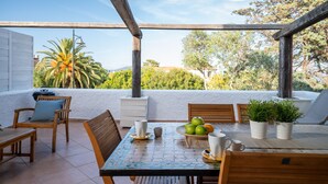 Une terrasse avec une table dressée pour le repas, entourée de chaises en bois et d’un banc.