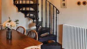 Una escalera de madera con barandillas negras ornamentadas, una mesa de comedor con sillas y un jarrón con flores.