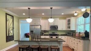 Una cocina con isla central, armarios blancos, electrodomésticos de acero inoxidable e iluminación colgante.