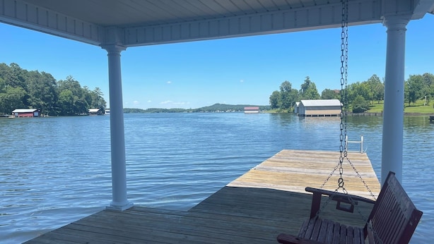 Un muelle de madera con una silla mecedora y una zona cubierta con vistas a un lago tranquilo.