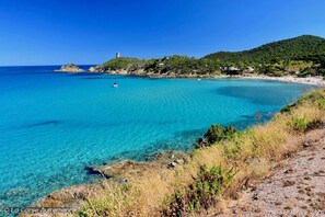 A coastal landscape with clear turquoise waters, rocky shorelines, and a lighthouse on a hill. - Corse Moriani-santa Maria Poggio Plaget2 Climatisé (Santa-Maria-Poggio)