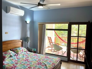 A bedroom with a bed, an air conditioner, a ceiling fan, a lamp, and a sliding glass door leading to an outdoor patio with chairs and a hammock. - Amazing view, steps to Ocotal beach, 3 Pools, Los Almendros #32 (Playa Ocotal)