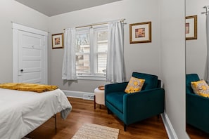 Une chambre à coucher avec un lit, deux chaises, une fenêtre avec des rideaux et une porte.