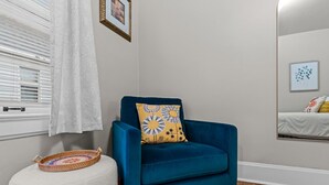 A room with a blue armchair, a small stool, a window with blinds, and a bed with a mirror. - Fully Fenced Yard, Dogs Welcome, Near MSU and Cox South (Springfield)