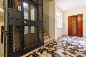 A room with a tiled floor, a wooden door, and a staircase leading to another level.