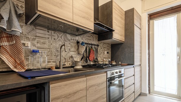 A modern kitchen with wooden cabinets, a built-in oven, and a large window. - Via Coriolano 8 - Three Bedroom Apartment, Sleeps 6 (Naples)