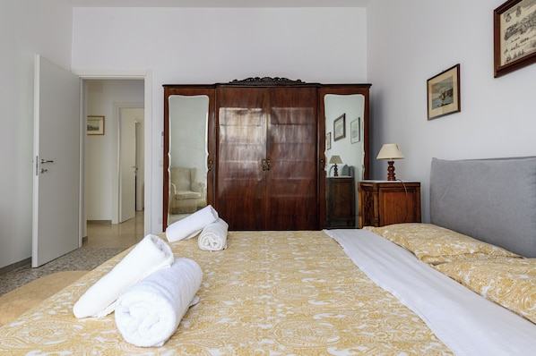 A hotel room with a bed, a wardrobe, a mirror, and a door leading to another room.