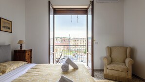 A bedroom with a bed, a chair, a balcony, and a view of buildings. - Via Coriolano 8 - Three Bedroom Apartment, Sleeps 6 (Naples)