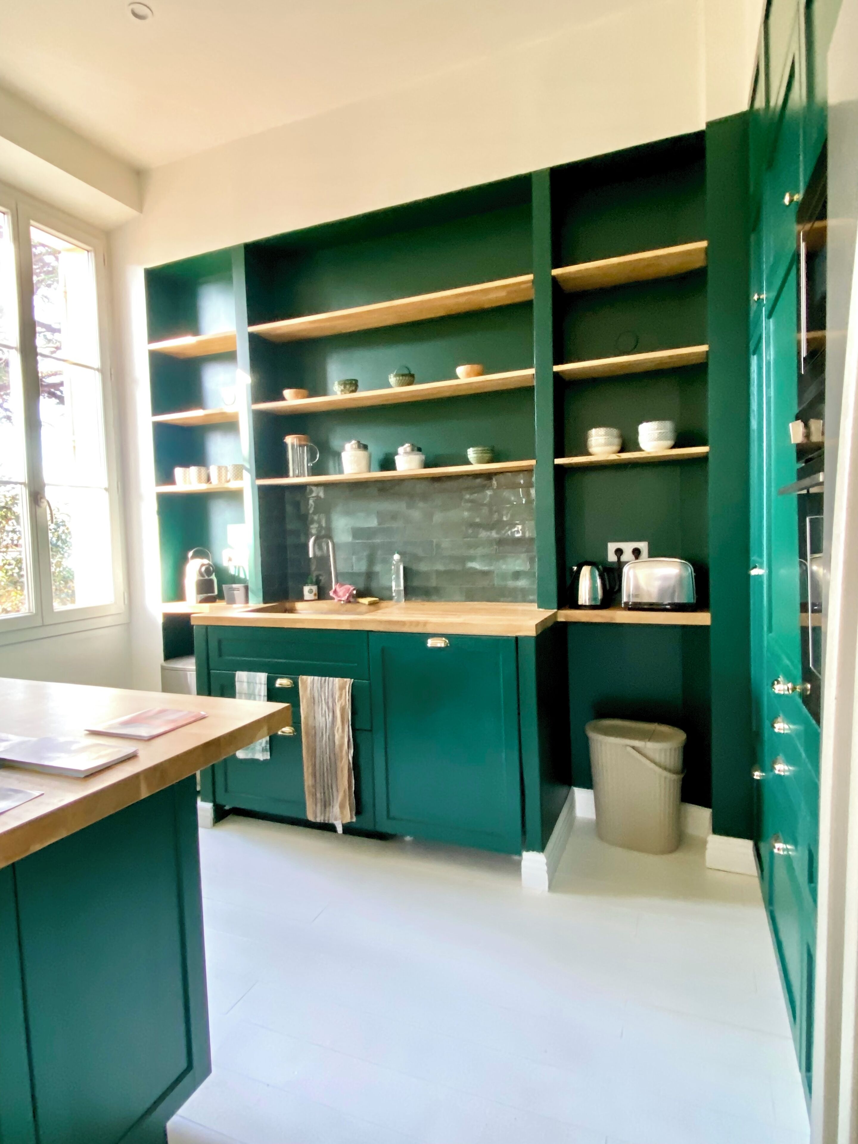 A kitchen with green cabinets, wooden shelves, and a white countertop.