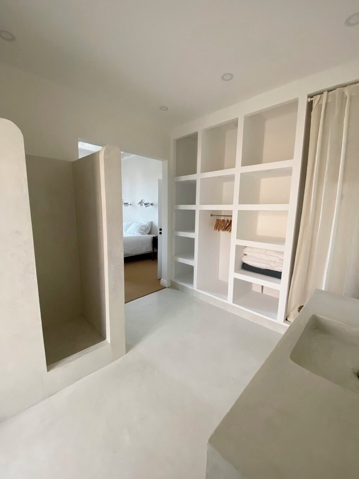 A spacious, modern room with a large white shelving unit, a built-in bench, and a view into another room with a bed.