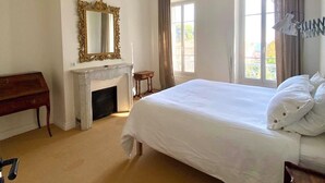 Un dormitorio con una cama grande, una chimenea, un espejo y una ventana con cortinas.