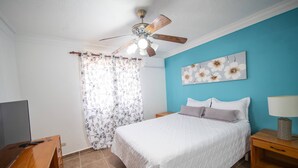 Une chambre à coucher avec un lit, des tables de chevet, un ventilateur de plafond, une télévision et un rideau à motifs floraux.
