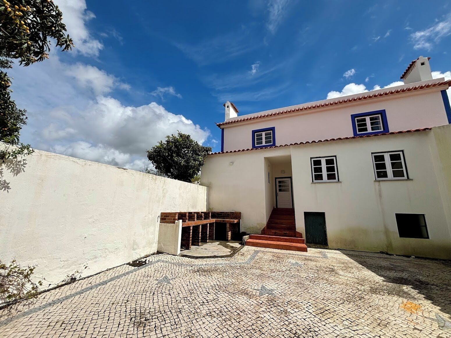 Um edifício de dois andares com fachada branca e molduras de janela azuis, entrada de tijolos e um pátio de paralelepípedos.