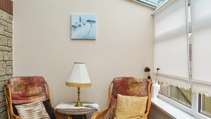 En hyggelig krog med to fletstole, et lille rundt bord, en lampe og et billede på væggen.