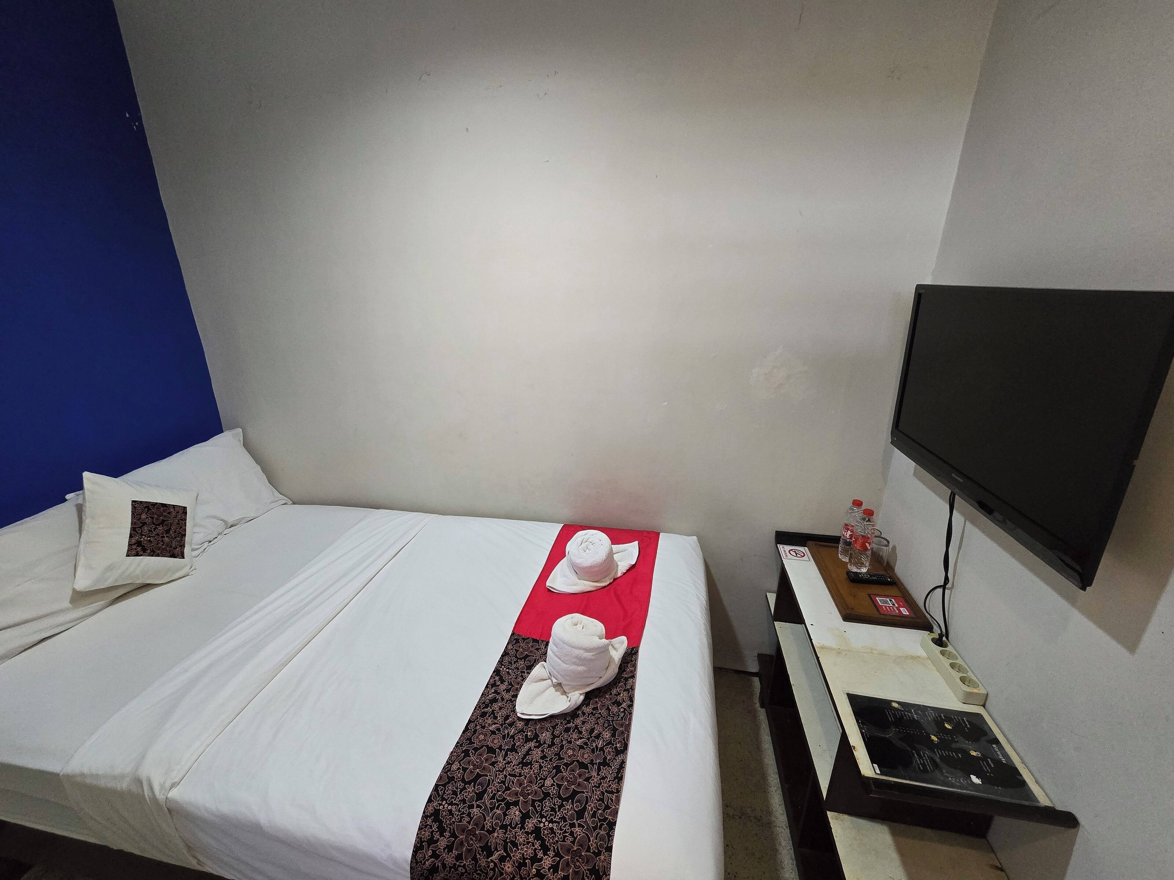 A hotel room with a bed, a flat-screen TV, a desk with a computer, and a wall-mounted TV.