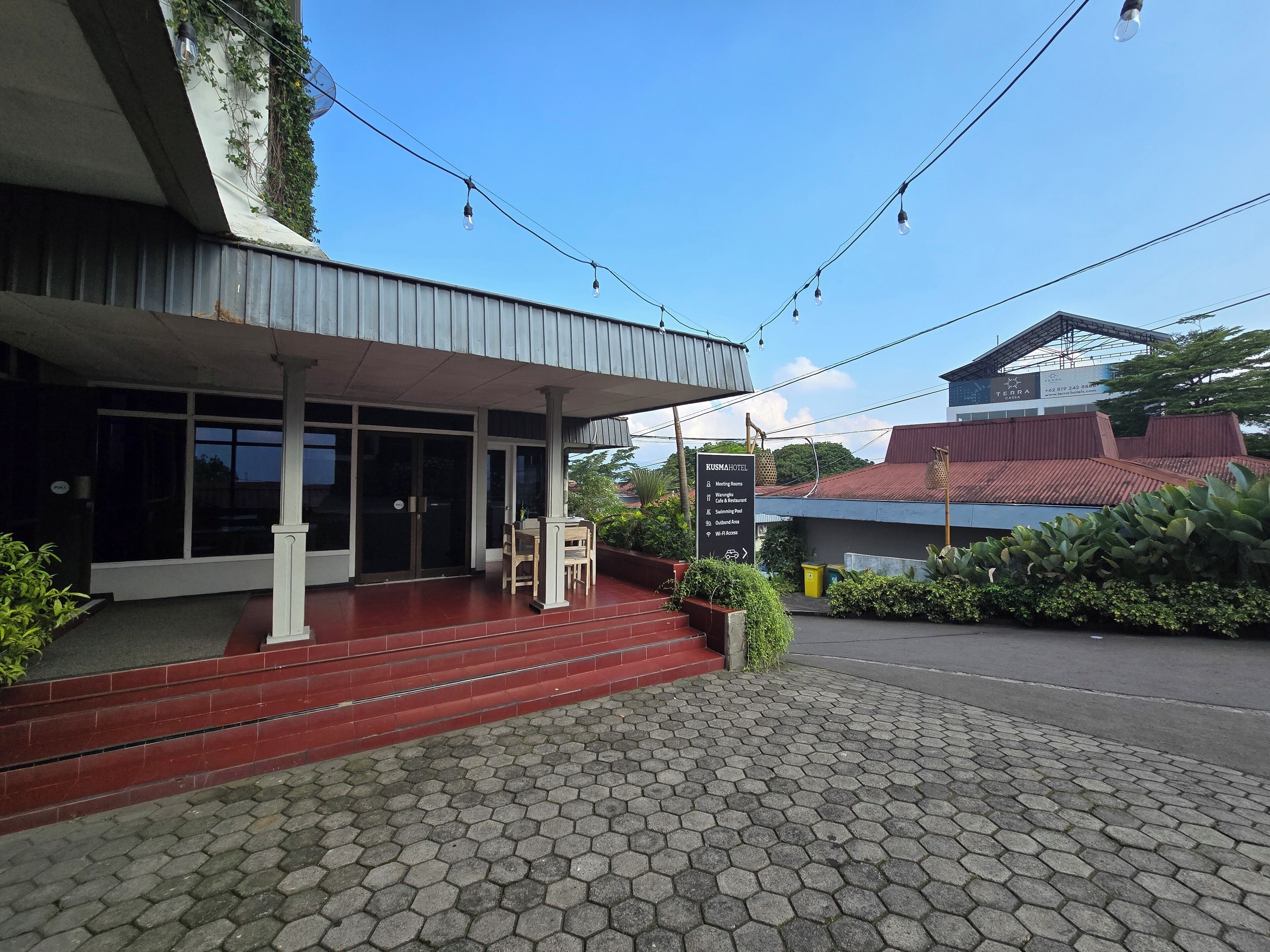A hotel entrance with a red brick pathway leading to a covered area with a table and chairs.