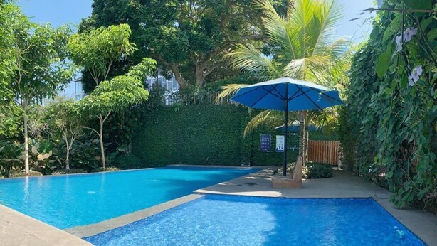 A swimming pool with a blue tiled edge, surrounded by lush greenery and a palm tree. - Kusma Hotel Bandungan Semarang (Bandungan)