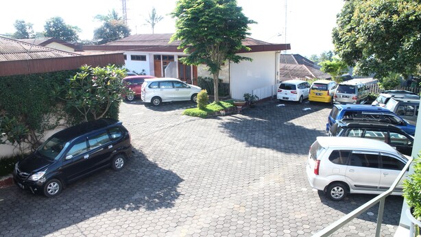 A parking area with multiple cars, a building with a red roof, and a tree in the center. - Kusma Hotel Bandungan Semarang (Bandungan)