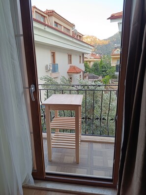 A balcony with a table and chair, a view of neighboring buildings, and a metal railing. - Mihenk Pansiyon (Marmaris)