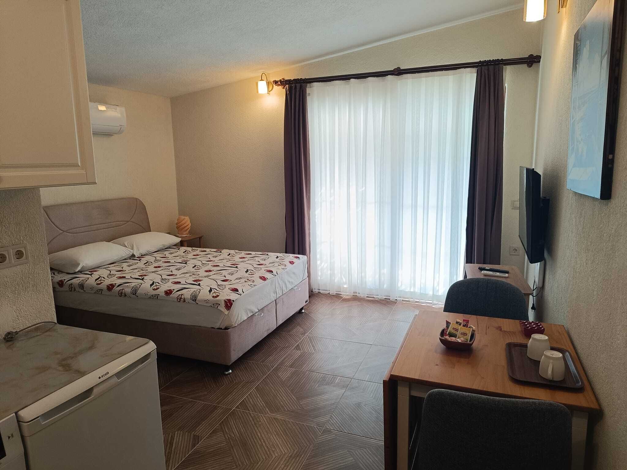 A hotel room with a bed, a desk, a chair, a TV, and a window with curtains.