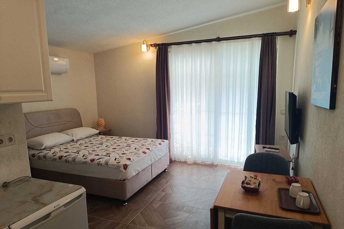 A hotel room with a bed, a desk, a chair, a TV, and a window with curtains.