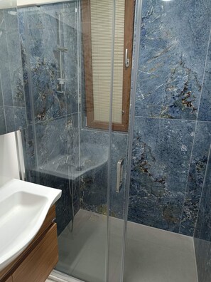 A bathroom with a glass-enclosed shower, a wooden vanity, and a marble-tiled wall. - Mihenk Pansiyon (Marmaris)