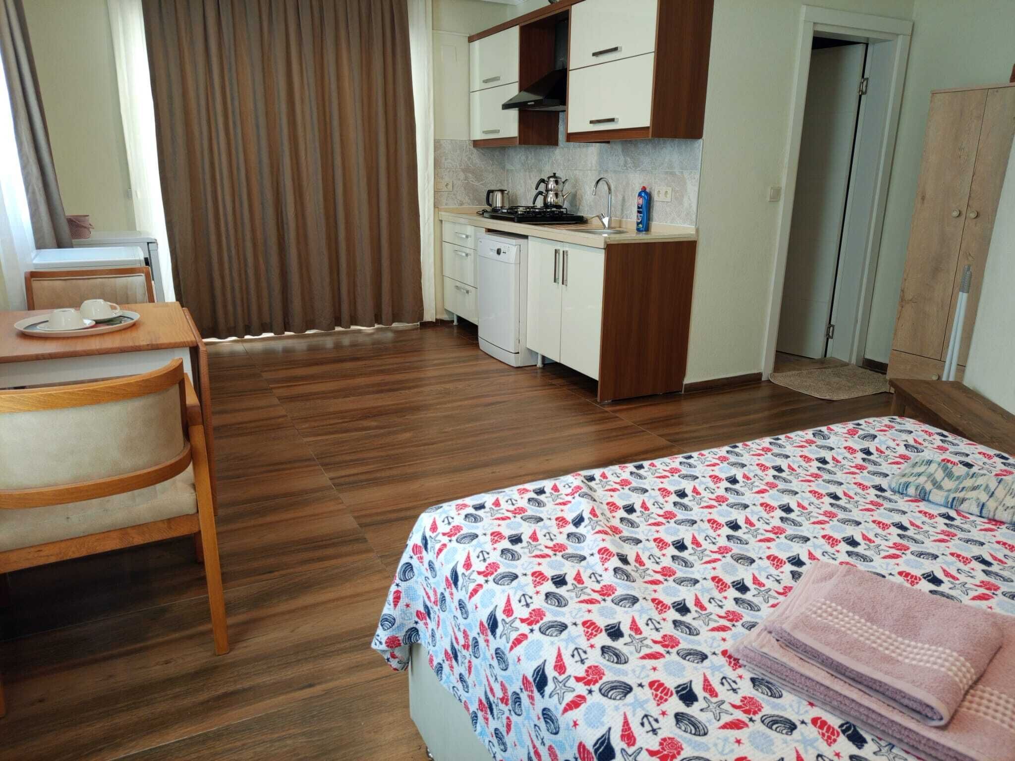 A compact hotel room with a bed, a small desk with a chair, a kitchenette, and a bathroom.