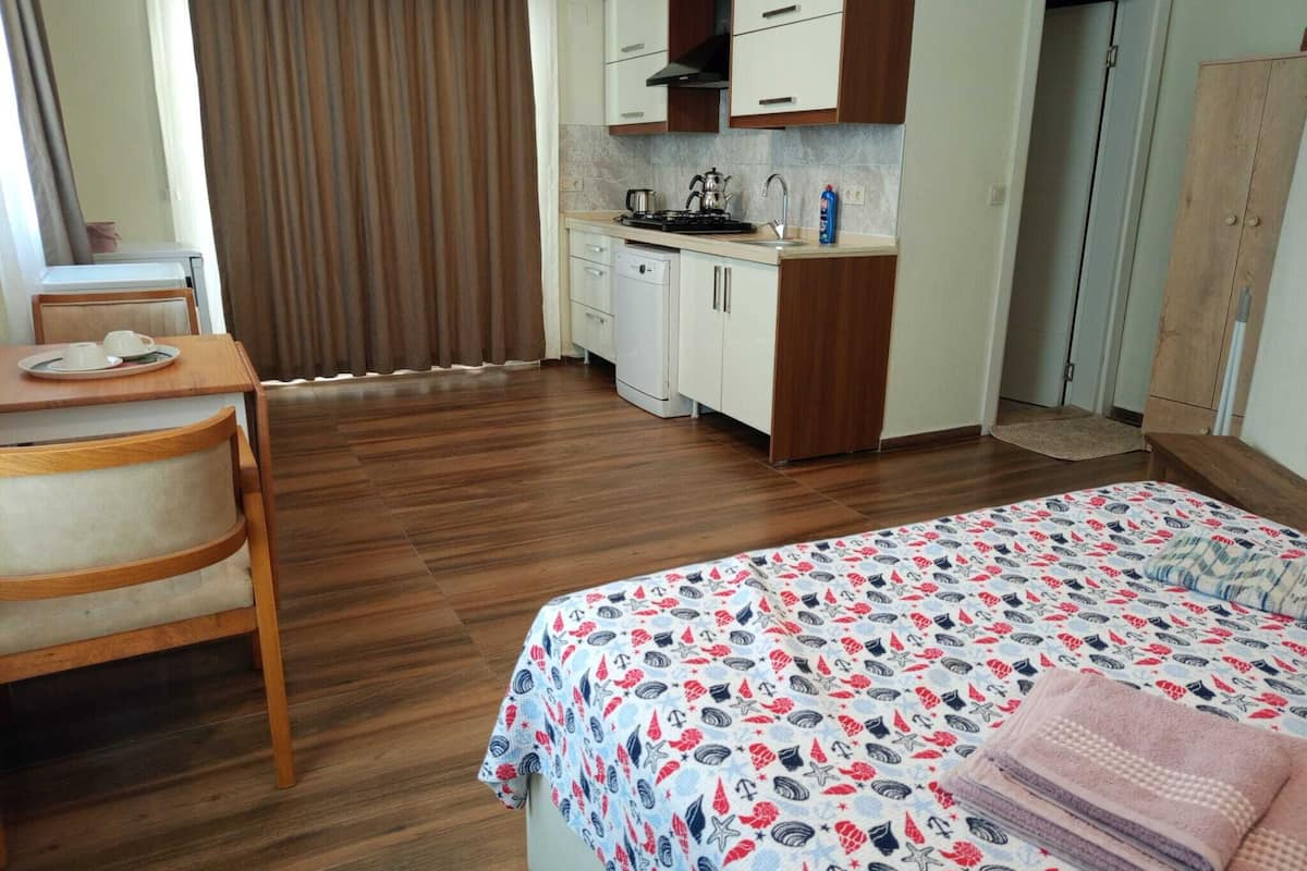 A compact hotel room with a bed, a small desk with a chair, a kitchenette, and a bathroom.