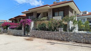Uma casa de dois andares com fachada de pedra, telhado ladrilhado e um muro de pedra na frente.