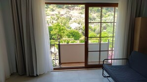 Quarto com cama, vista para uma varanda através de uma porta de correr de vidro e janela com cortinas.