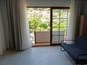 A room with a bed, a view through a sliding glass door to a balcony, and a window with curtains. - Mihenk Pansiyon (Marmaris)