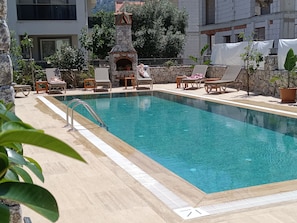A swimming pool with lounge chairs and a stone fireplace. - Mihenk Pansiyon (Marmaris)