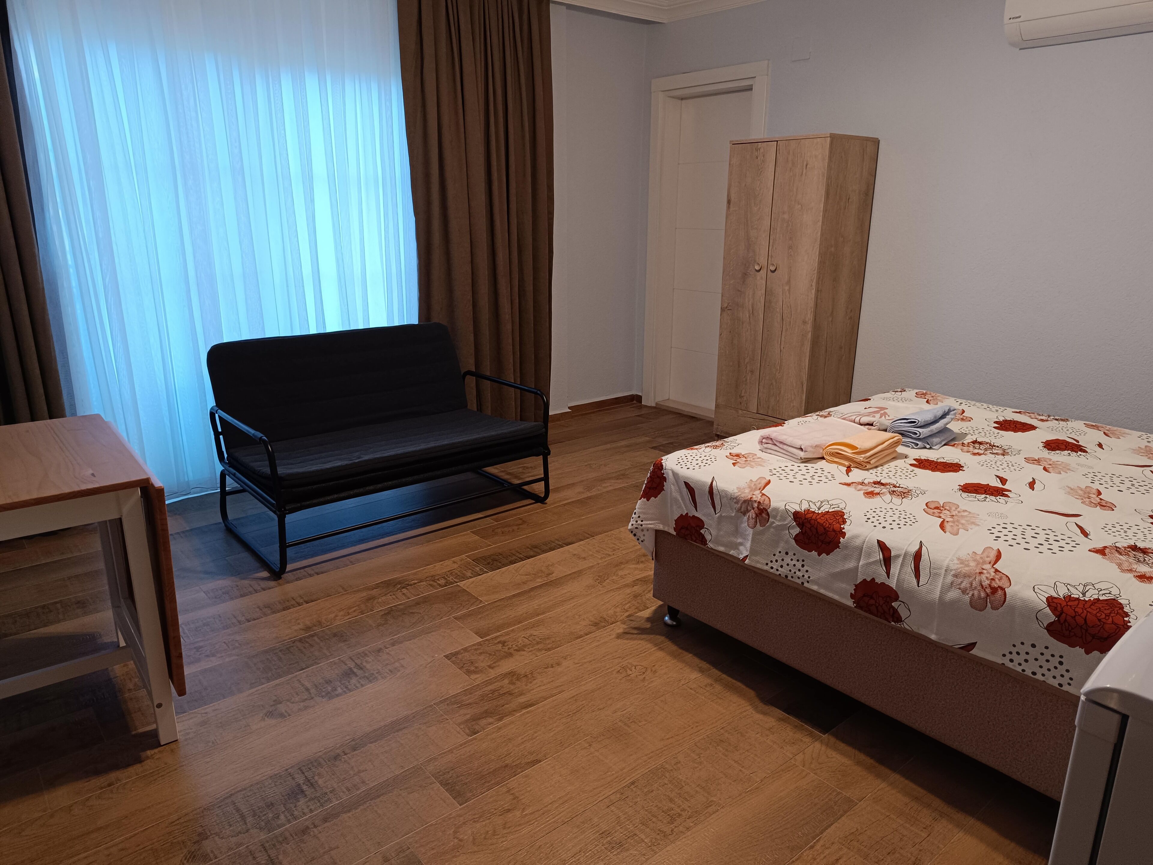A room with a bed, a sofa, a wardrobe, and a table.