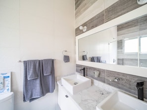 A modern bathroom with two sinks, a large mirror, and towels hanging on a rack.
