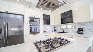 Una cocina moderna con refrigerador de acero inoxidable, horno empotrado, estufa a gas y cafetera.