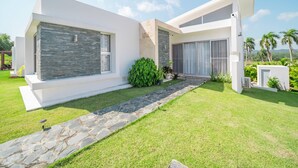 Una casa moderna con un sendero de piedra que conduce a la entrada, rodeada de abundante vegetación y palmeras.