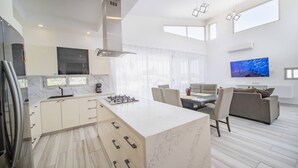 Una cocina moderna con una isla central, un comedor con televisor y una sala de estar con sofá.