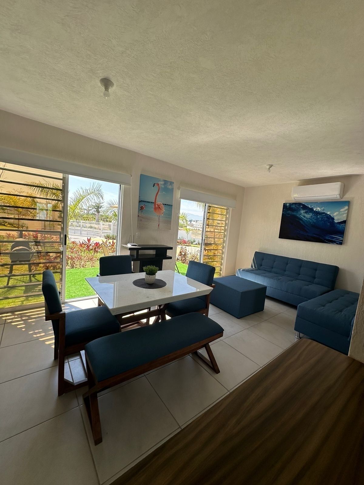 A modern living room with a dining area, large windows, and a view of a garden.