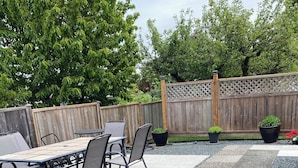 Een terras buiten met een tafel en stoelen, omgeven door een houten hek en beplanting.
