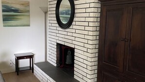 Een woonkamer met een schouw van baksteen, een ronde spiegel, een klein tafeltje en een donker houten kast.