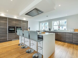 Een moderne keuken met een centraal eiland, barkrukken en een inbouwoven.